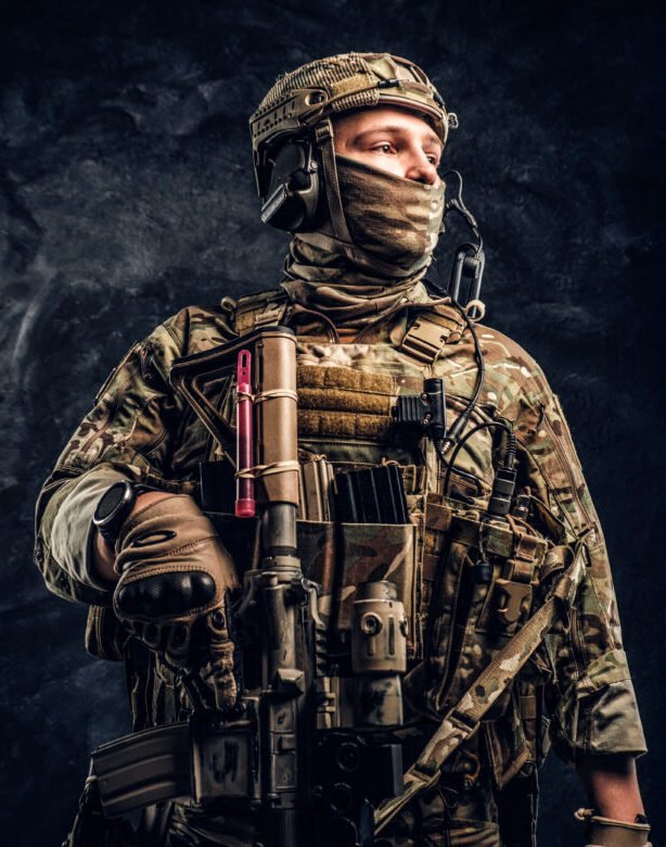 Modern special forces soldier in camouflage uniform looking sideways. Studio photo against a dark textured wall.